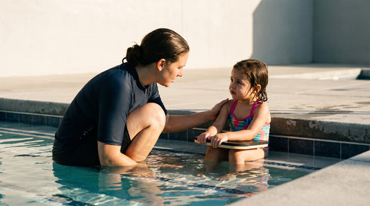 Swim instructor gently reassuring a hesitant child on the pool steps in the shallow end