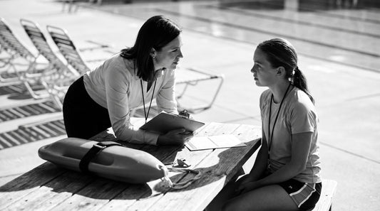 Aquatics manager interviewing a lifeguard candidate at a poolside table with application forms