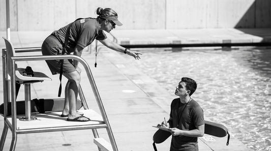 Certified lifeguard on the stand supervising a trainee guard observing from the deck