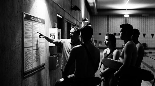 Aquatics team reviewing an emergency action plan on the pool deck near an AED cabinet