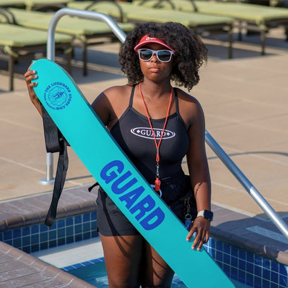 The Lifeguard Store 50" turquoise rescue tube with blue "GUARD" lettering, held by a lifeguard in a black swimsuit.