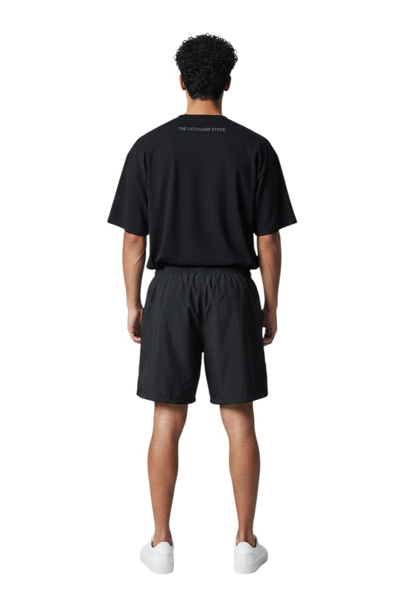 The Lifeguard Store black polyester board shorts with elastic waistband and 7" inseam. Ideal for water activities.