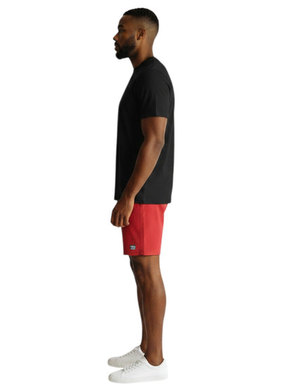 A man wearing a black The Lifeguard Store short sleeve crew neck rashguard and red shorts, side profile view.