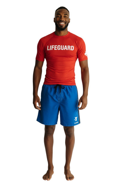 The Lifeguard Store blue polyester board shorts with black side stripes and YMCA Guard logo. Elastic waistband, drawstring, and side pocket.