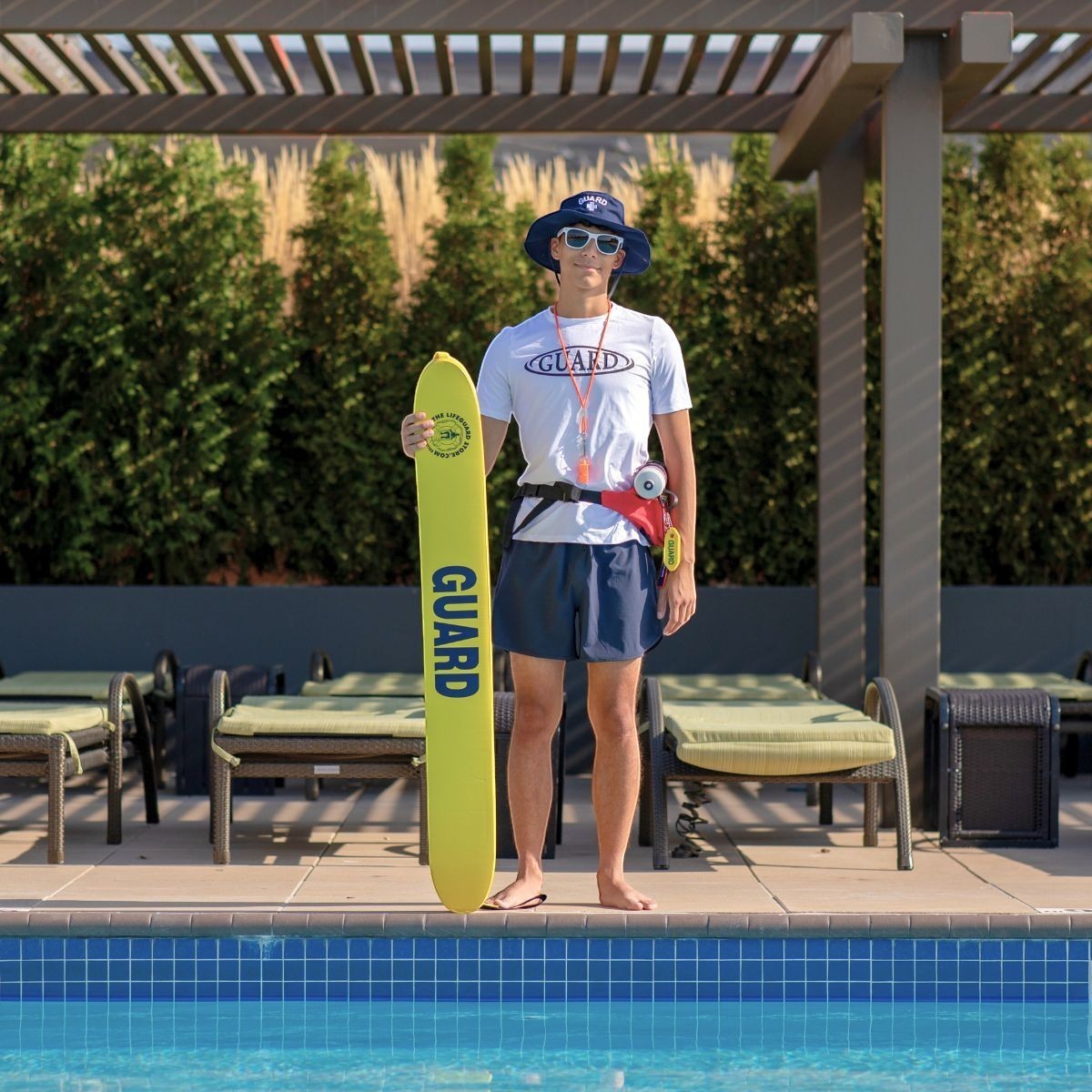 The Lifeguard Store Men's navy blue 5" lined lifeguard shorts with elastic waistband and drawstring. Model holds yellow rescue tube.