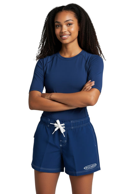 The Lifeguard Store navy blue polyester-spandex blend board shorts with white drawstring and contrast stitching. Features GUARD logo on left thigh.