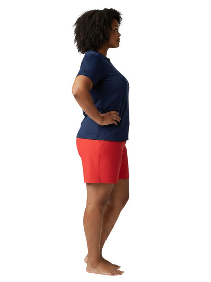 A model wearing The Lifeguard Store navy blue short sleeve crew neck rashguard with red shorts, side profile view.