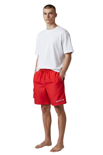 The Lifeguard Store red polyester board shorts with liner, elastic waistband, drawstring, and "INSTRUCTOR" text.