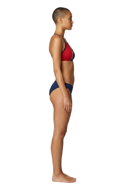 Model wearing The Lifeguard Store RISE Guard red and navy blue splice bikini with flat-locked seams, side view