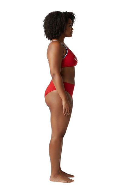 A model wearing The Lifeguard Store tri-color red bikini with white and blue trim, side view, studio background.