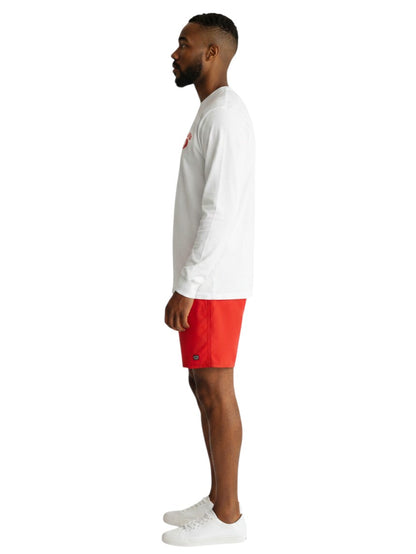 The Lifeguard Store white long sleeve cotton guard t-shirt with red logo, worn by a man in red shorts, side view.